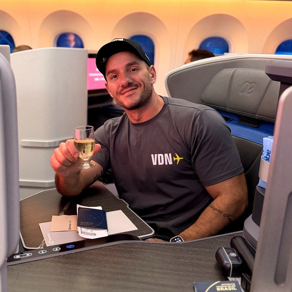 Adriano Brandão sorrindo e fazendo um brinde a bordo, com a camiseta do Viajando de Novo
